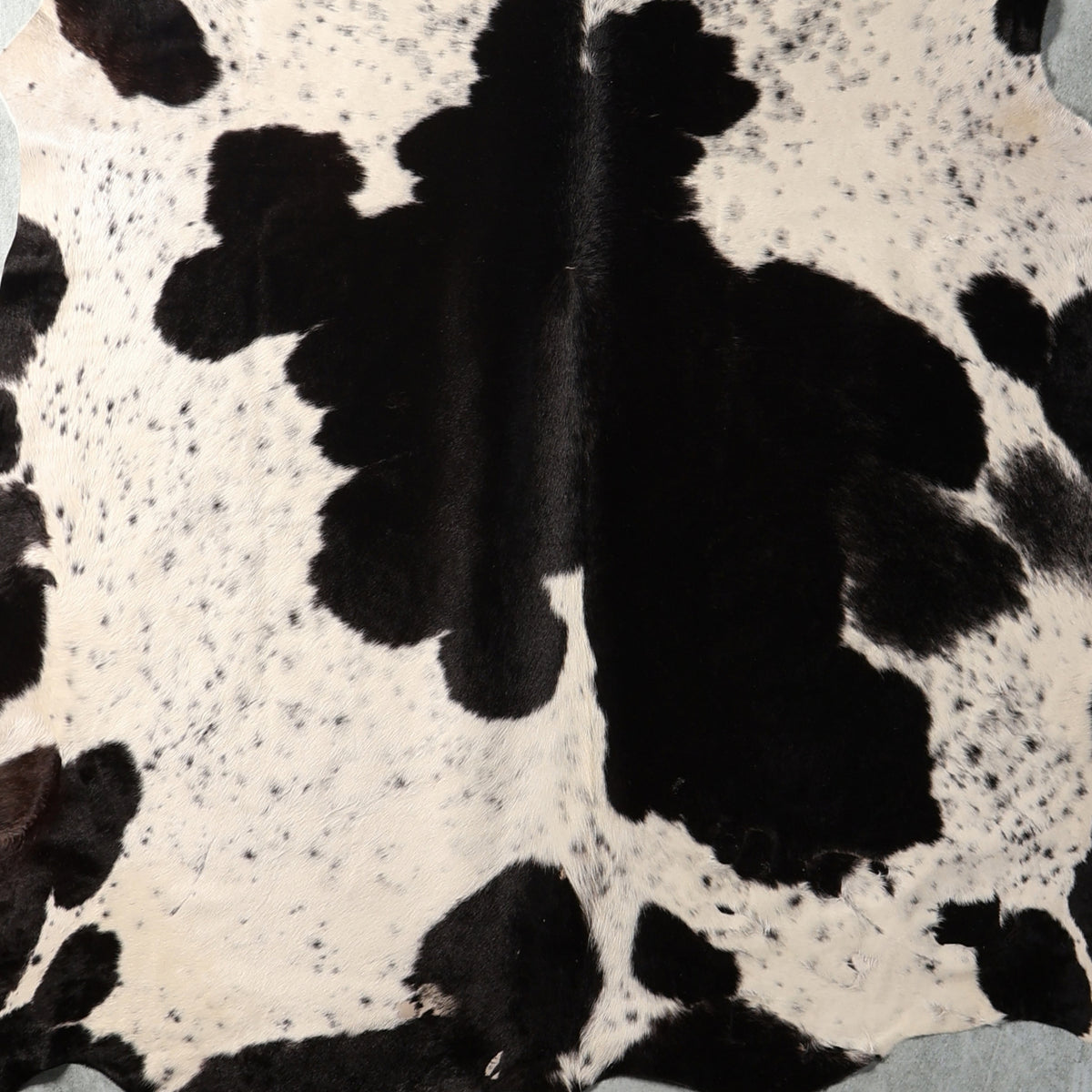 Black and white cowhide rug with natural spotted pattern and visible hair texture.