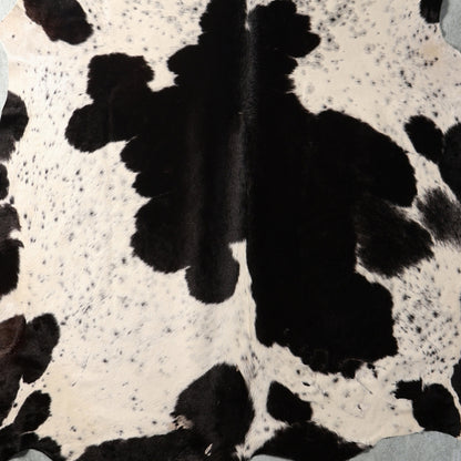 Black and white cowhide rug with natural spotted pattern and visible hair texture.