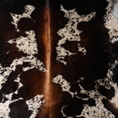 A close-up of a tri colour cowhide rug showing a natural black and brown pattern with a lighter tan streak running vertically through the center.